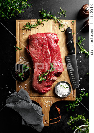 Beef meat entrecote on a cutting board, raw beef meat fillet on black background, top view 111320518