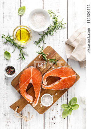 Fresh raw salmon steaks on a board with ingredients for cooking, top view Fresh raw salmon steaks on a board with ingredients for cooking, top view 111320521