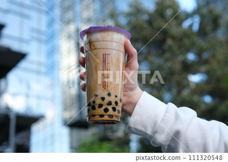 A glass of Bubble Tea delicious tea drink against the backdrop of skyscrapers in a girl's hand shake and stir enjoy the summer Cold drinks in Canada Vancouver in traditionally buy. High quality A glass of Bubble Tea delicious tea drink against the backdrop of skyscrapers in a girl's hand shake and stir enjoy the summer Cold drinks in Canada Vancouver in traditionally buy. High quality 111320548