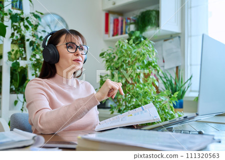 Woman teacher in headphones with textbook working online using computer 111320563