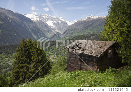 Old wooden shed with a hole in de wooden tile roof looking out over the valley 111321443