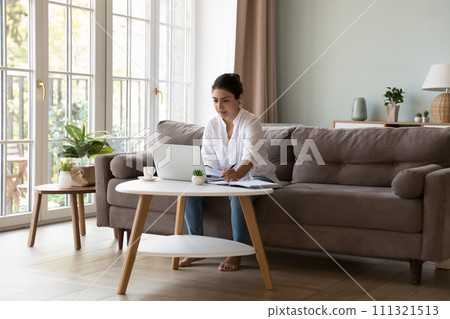 Thoughtful Indian woman writes ideas seated at table with laptop Thoughtful Indian woman writes ideas seated at table with laptop 111321513
