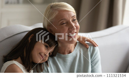 Cute little girl hugging smiling senior grandmother, sitting on couch Cute little girl hugging smiling senior grandmother, sitting on couch 111321534