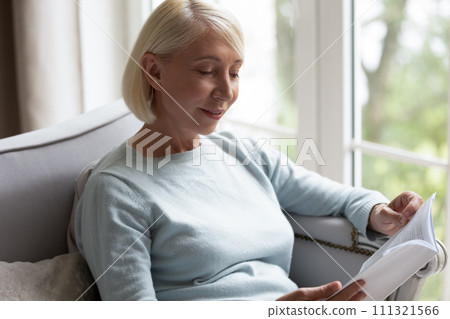 Smiling mature woman reading book, sitting on couch at home 111321566