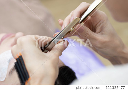 Beauty concept. Cosmetology. Eyelash extensions. A beautiful girl lies on the sofa in a beauty salon. Master, specialist doing eyelash extensions. Beauty concept. Cosmetology. Eyelash extensions. A beautiful girl lies on the sofa in a beauty salon. Master, specialist doing eyelash extensions. 111322477