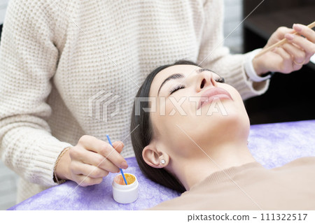 Beauty concept. Eyelash extensions. A beautiful girl lies on a couch in a beauty salon. The master does eyelash extensions. 111322517