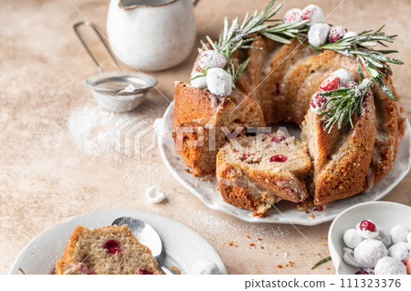 Christmas bundt cake decorated with glaze, cranberries and rosemary served on beige table. Homemade cake recipe 111323376