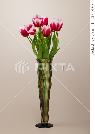 Flowers in a vase. Bouquet of beautiful tulips in a tall figured vase on a beige background. 111323470