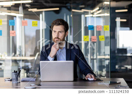 Focused mature businessman working intently in a modern office with sticky notes on glass. Concept of leadership and professionalism. Focused mature businessman working intently in a modern office with sticky notes on glass. Concept of leadership and professionalism. 111324150