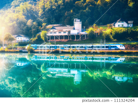 Blue modern high speed train and river in green forest at sunrise 111324204