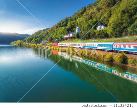 Aerial view of speed train moving near river in alpine mountains 111324213