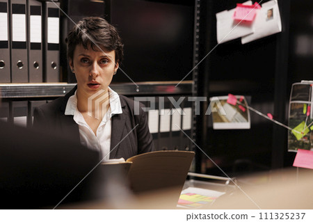 Criminology department employees discussing criminal case, analyzing mysterious missing person case. Private detective discussing suspect report with police officer, working overtime in arhive room 111325237