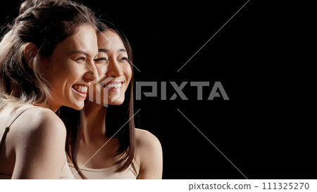 Diverse happy girls hugging each other in beauty ad, feeling flawless and cheerful about skincare campaign. Two beautiful women posing on camera promoting body acceptance and diversity. 111325270