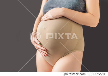 Pregnant bliss: Mom-to-be embraces her baby bump with a soft fabric bandage, providing gentle support. Maternity made comfortable 111325591