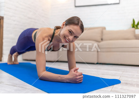 Slim young woman standing in plank on a blue mat Slim young woman standing in plank on a blue mat 111327097