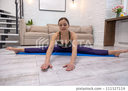Young yogini sitting in a split while doing yoga at home Young yogini sitting in a split while doing yoga at home 111327119