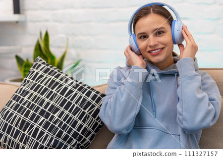 Young girl listening music while sitting on sofa in living room. Young girl listening music while sitting on sofa in living room. 111327157