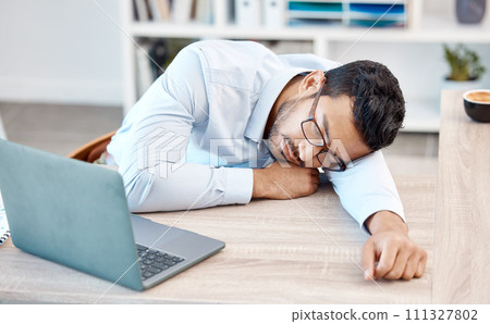 Tired, headache and sleeping worker behind laptop while lying his head on his desk in his office. Stress, burnout and chronic fatigue with young professional male feeling exhausted and overworked 111327802