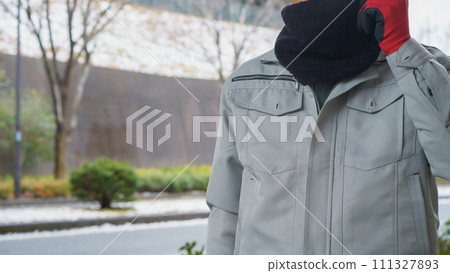 在雪景中，一名穿著工作服的男子使用頸部保暖器來保護自己免受寒冷 111327893