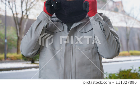 A snowy scene with a man in work clothes using a neck warmer to protect himself from the cold 111327896