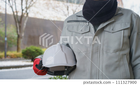 A snowy scene with a man in work clothes using a neck warmer to protect himself from the cold 111327900