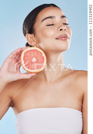 Grapefruit, woman skincare and wellness fruit for face grooming, wellness and diet health on a blue background in studio. Happy, smile and beauty brazilian model with vitamin c food product in hands 111328462