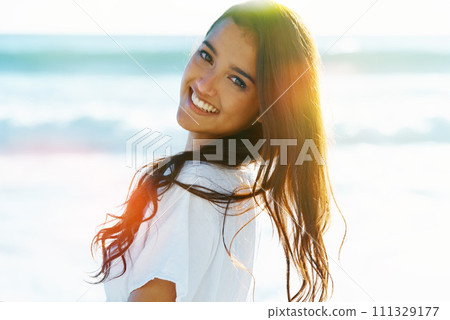 Smile, portrait and woman on beach with flare, waves and sunset on summer holiday at sea in Hawaii. Smile, sun and face of girl on ocean vacation with adventure, travel and relax on tropical island. 111329177