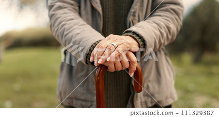 Senior cane, hands and person in nature for walking, relax and in a park for peace. Closeup, standing and an elderly woman in a garden or natural environment for wellness with a stick for support 111329387