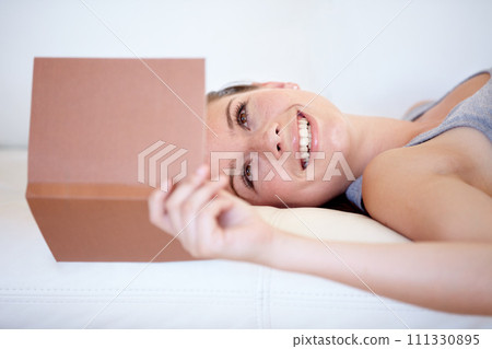 Book, smile and a woman reading on a sofa in the living room of her home on the weekend for leisure. Relax, novel or literature with a happy young person in her apartment for a storytelling hobby 111330895