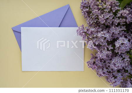 Composition with empty violet envelope and beautiful spring lilac flowers on beige background. Mockup card invitation greeting card postcard copy space template. Branches of lilac blooming bouquet.  111331170