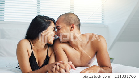 Happy couple, relax and kissing on bed for intimacy, morning romance or love in embrace, trust or care at home. Young man and woman smile lying in bedroom for passion or bonding together at house 111331700