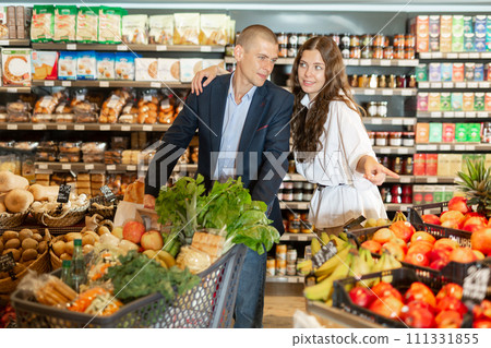 Portrait of a happy young couple in a supermarket with a full grocery cart Portrait of a happy young couple in a supermarket with a full grocery cart 111331855
