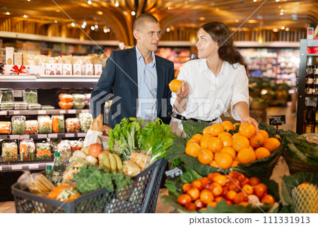 Happy young couple with a grocery cart in the supermarket shooses tangerines 111331913