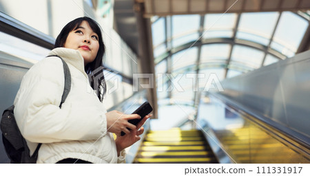 Woman, stairs and smartphone for commute, texting and japanese on social media app. Technology, communication and text message for digital, internet and chatting with backpack, travel and escaltor 111331917