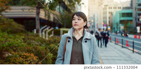 Woman, Asian and walking, travel or commute to work with professional in city with earphones. Listening to music on journey, podcast and commuter on urban street or sidewalk in Tokyo with playlist 111332004