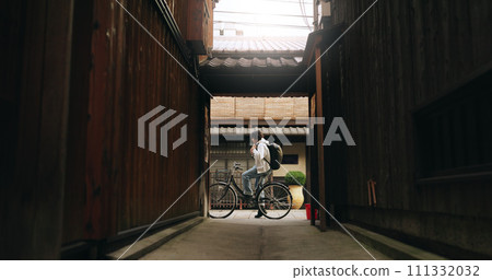 Bicycle, travel and man riding by building for exercise or transportation to college academy. Fitness, backpack and young male student driving a bike to university for carbon footprint by houses. Bicycle, travel and man riding by building for exercise or transportation to college academy. Fitness, backpack and young male student driving a bike to university for carbon footprint by houses. 111332032