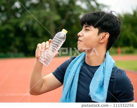 Asian Male Athlete Taking a Refreshing Water Break on Track Field; Active and Hydrated in action 111332256