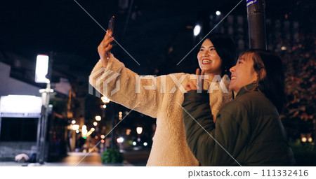 Japanese, women and selfie outdoor at night with hand gesture, peace sign and happy in city street. Friends, people and phone with smile for travel, adventure and social media update in urban town 111332416