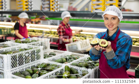 Positive woman with avocado slices in hands at food factory warehouse Positive woman with avocado slices in hands at food factory warehouse 111332584
