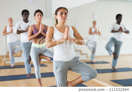 Latin american girl in Eka Pada Pranamasana during group yoga training Latin american girl in Eka Pada Pranamasana during group yoga training 111332804