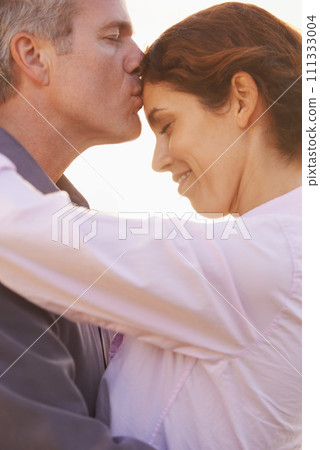 Couple, forehead kiss and hug with love, respect or happiness on holiday in retirement. Mature, man and woman embrace together outdoor at sunset on vacation or show affection or gratitude in marriage Couple, forehead kiss and hug with love, respect or happiness on holiday in retirement. Mature, man and woman embrace together outdoor at sunset on vacation or show affection or gratitude in marriage 111333004