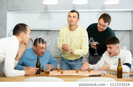 Group of cheerful men engaged in alcohol-fueled board game Group of cheerful men engaged in alcohol-fueled board game 111333016