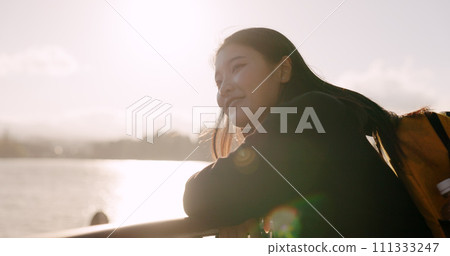 Japanese woman, lake and backpack with thinking, smile and sunrise on adventure, trip or vacation. Girl, person and happy for holiday with bag, vision and memory by water, river and bridge in Tokyo 111333247