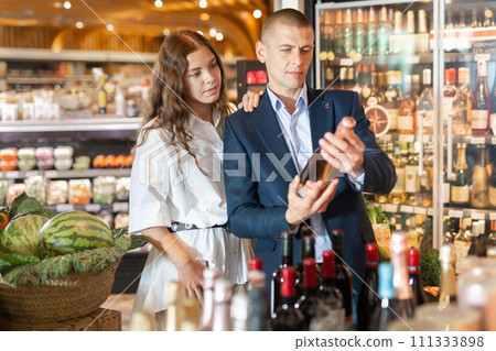 Young couple in the supermarket chooses a bottle of champagne 111333898