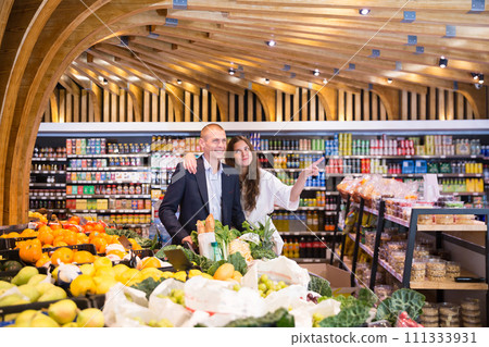 Portrait of a happy young couple with products in a cart in the supermarket Portrait of a happy young couple with products in a cart in the supermarket 111333931
