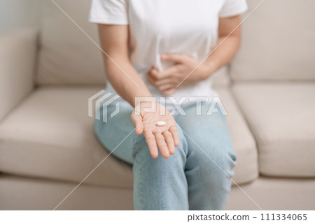 woman hand holding medicine painkiller pill and water glass on the sofa at home, taking for headaches,  stomach ache, Diarrhea Pain from food poisoning, Endometriosis, Hysterectomy and Menstrual 111334065