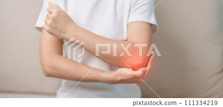 Woman having elbow ache during sitting on couch at home, muscle pain due to lateral epicondylitis or tennis elbow. injury, Health and medical concept Woman having elbow ache during sitting on couch at home, muscle pain due to lateral epicondylitis or tennis elbow. injury, Health and medical concept 111334219