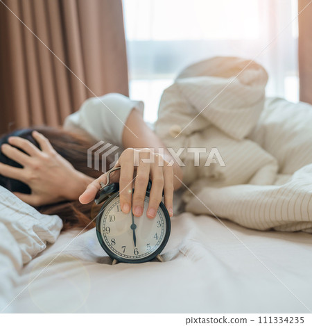 alarm clock and asian woman hand stop time in bed while sleeping, young adult female wake up late in the early morning. Relaxing , sleepy, daily routine and have a nice day concepts alarm clock and asian woman hand stop time in bed while sleeping, young adult female wake up late in the early morning. Relaxing , sleepy, daily routine and have a nice day concepts 111334235