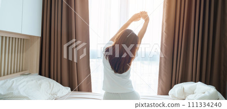happy woman stretching on bed after wake up, young adult female rising arms and looking to window in the early morning. fresh relax and have a nice day concepts happy woman stretching on bed after wake up, young adult female rising arms and looking to window in the early morning. fresh relax and have a nice day concepts 111334240