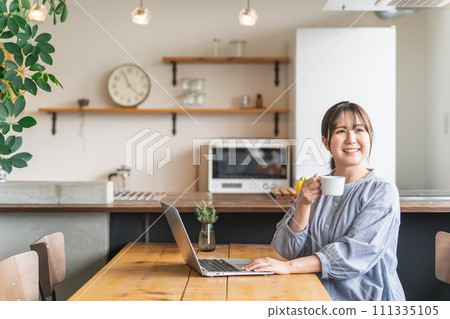 A woman using a computer while drinking coffee at home (online shopping, watching movies, streaming) A woman using a computer while drinking coffee at home (online shopping, watching movies, streaming) 111335105